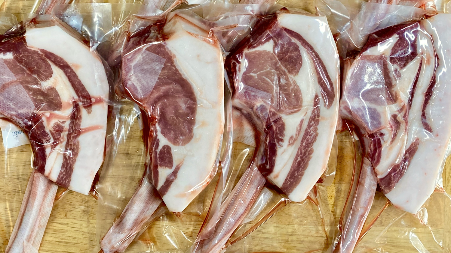 8 individually packaged Mangalitsa tomahawk-style Pork Chops from Blue Dirt Farms arranged on a wood butcher block surface.