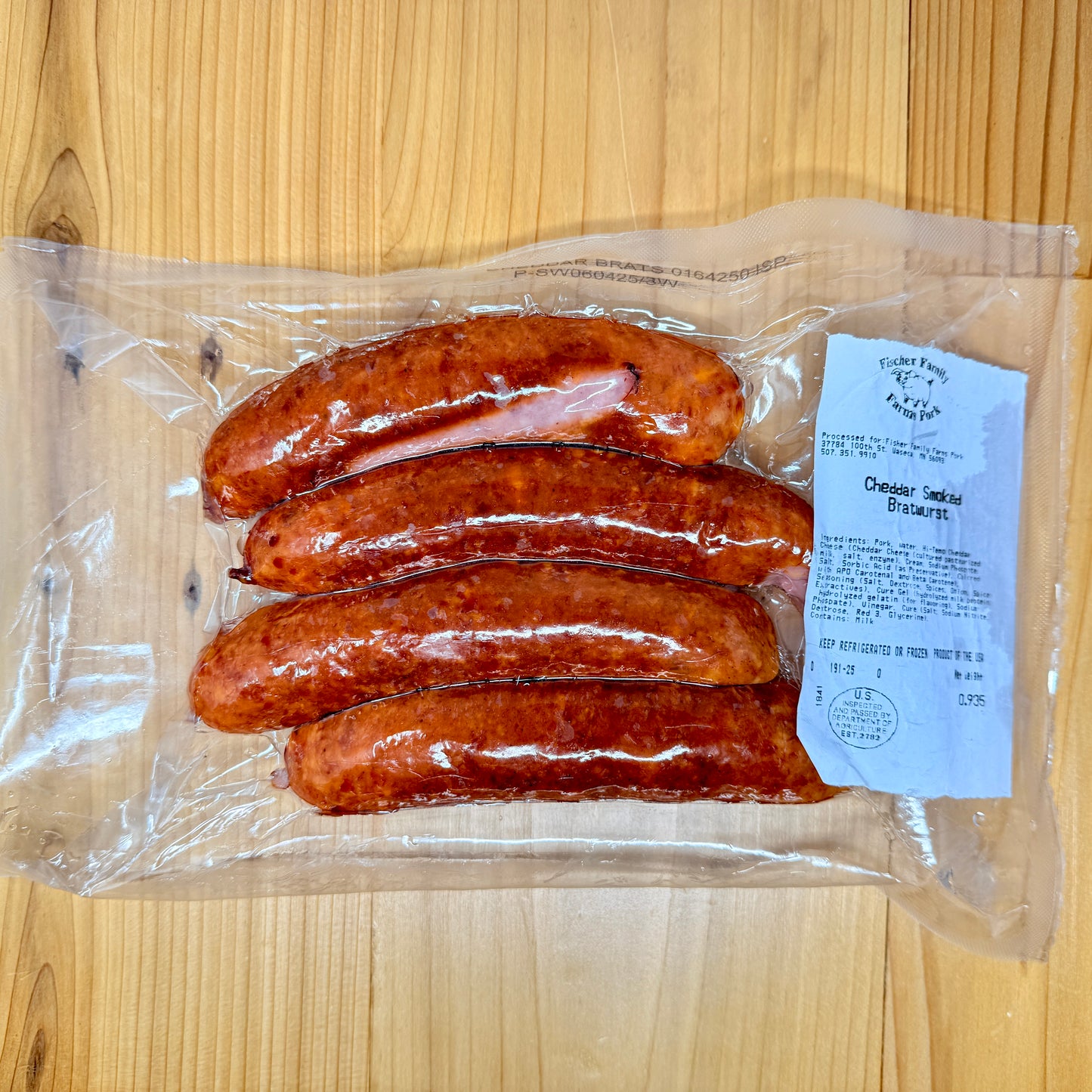 A package of 4 Cheddar Smoked Brats from Fischer Family Farms on a wooden surface