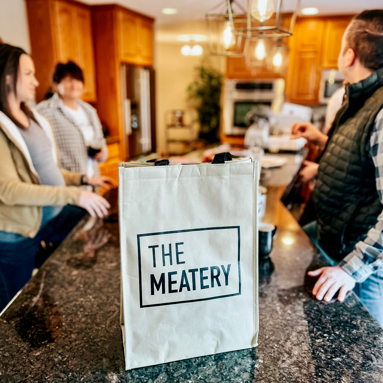 Members of The Meatery's team standing around a kitchen counter with a reusable "The Meatery" branded bag on the counter in the center of the image.