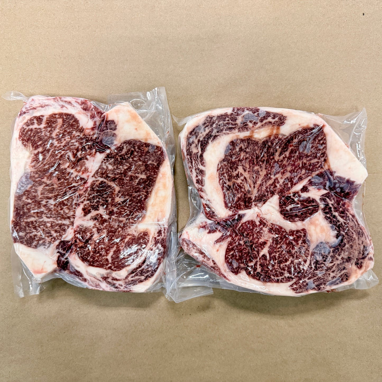 Two 2-packs of well-marbled boneless ribeye steaks from Backstreet Market on a brown butcher paper background