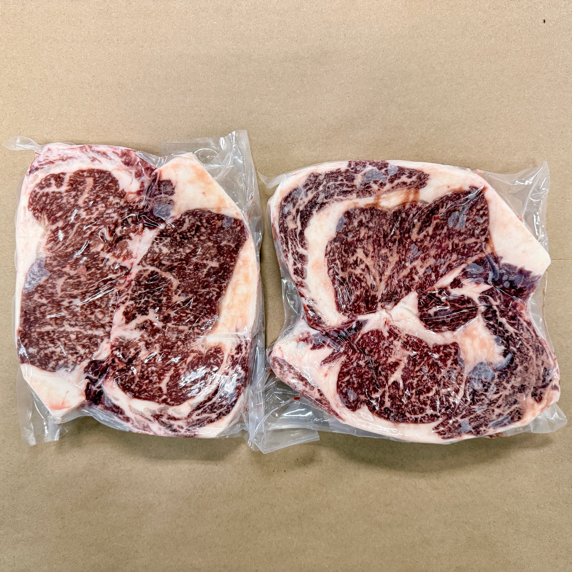 Two 2-packs of well-marbled boneless ribeye steaks from Backstreet Market on a brown butcher paper background