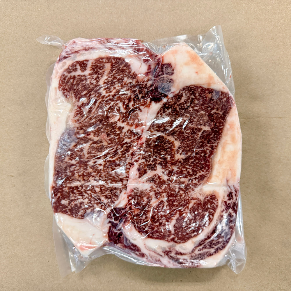 Two 2-packs of well-marbled boneless ribeye steaks from Backstreet Market on a brown butcher paper background