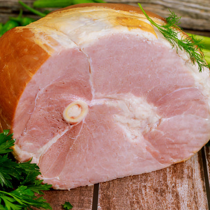 A sliced, bone-in ham sitting on a wood board with parsley and dill garnish.