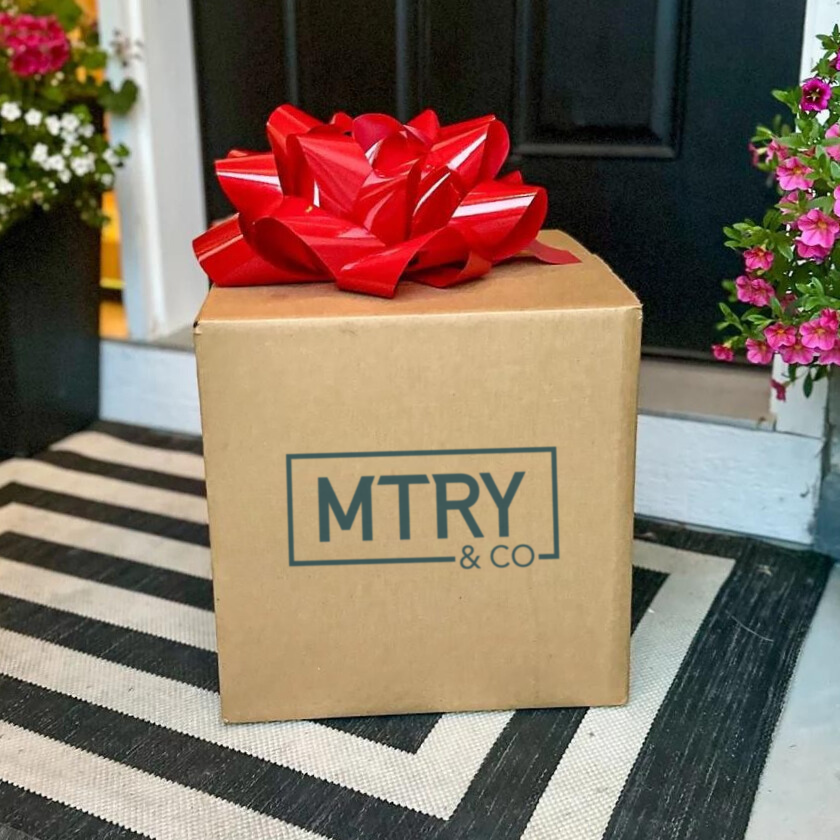 Cardboard box with a red bow on a doormat, featuring the brand 'MTRY & CO'.