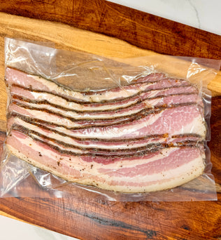Vacuum-sealed package of thick-cut black pepper bacon from MTRY & CO on a wooden cutting board