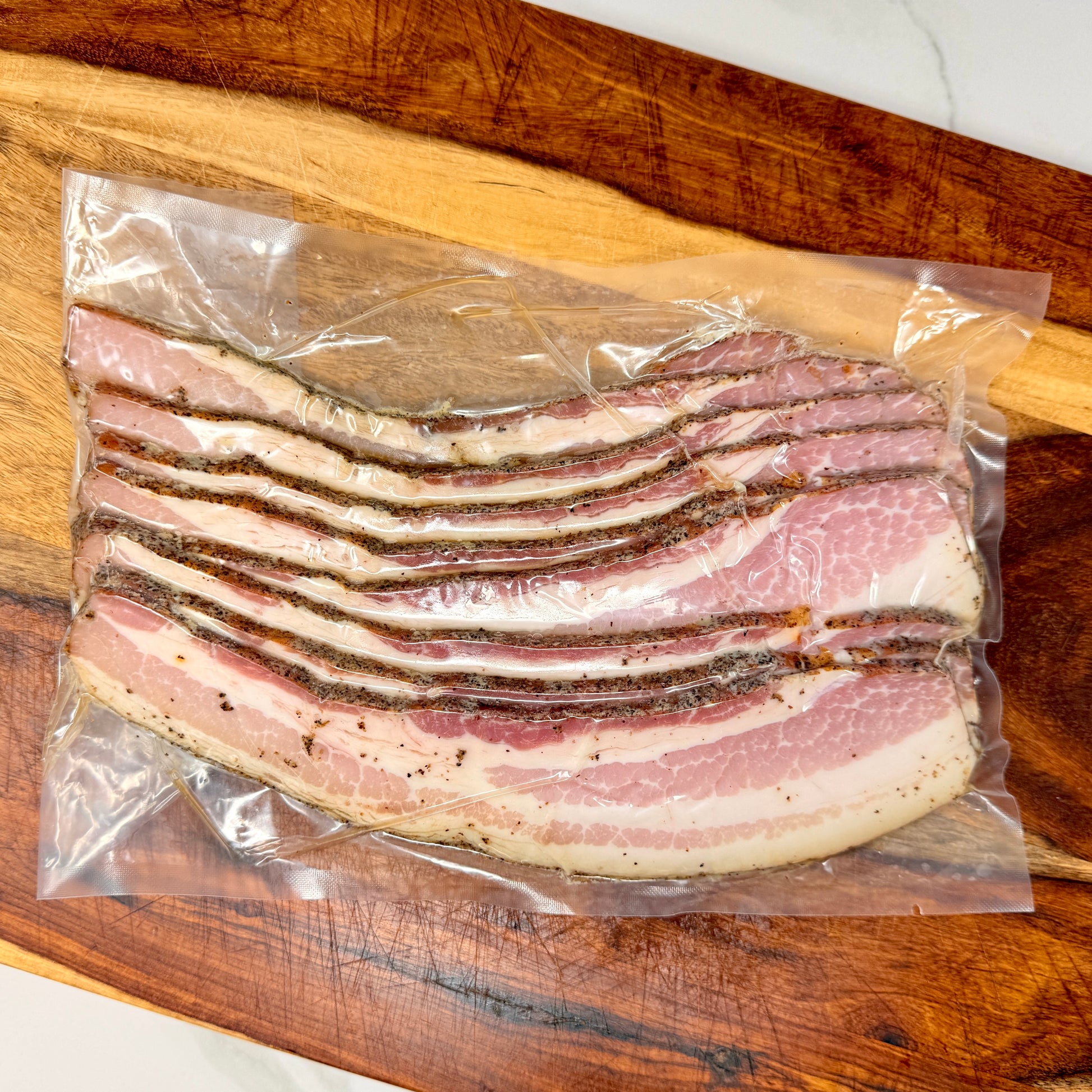 Vacuum-sealed package of thick-cut black pepper bacon from MTRY & CO on a wooden cutting board