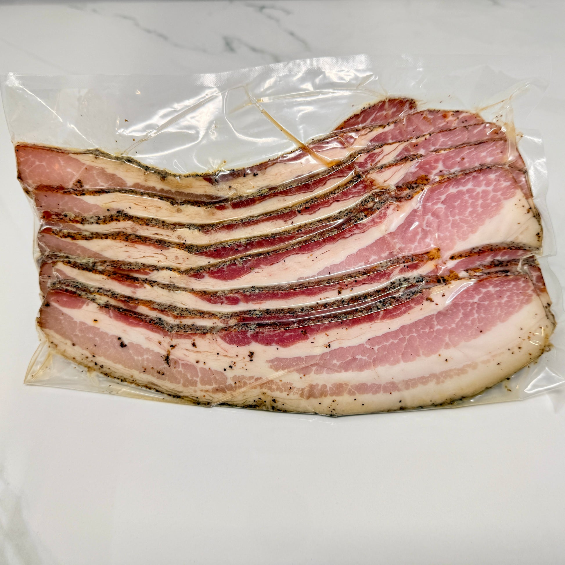 Vacuum-sealed package of thick-cut black pepper bacon from MTRY & CO on a wooden cutting board