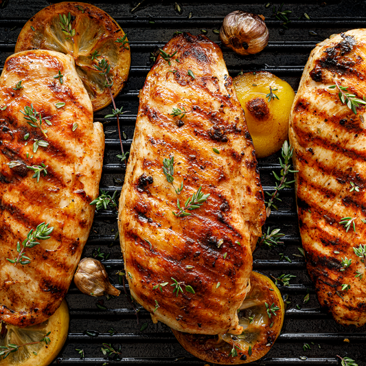 Grilled chicken breasts with lemon slices and herbs on a grill