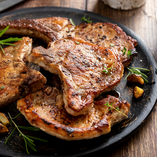 Seared pork chops on a black plate with rosemary sprigs on a wooden surface