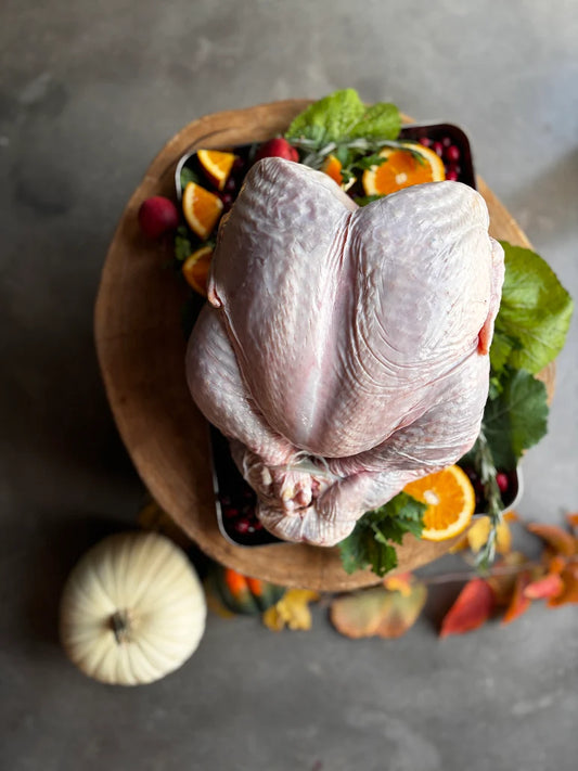 Raw turkey on a wooden board with fruits and vegetables on a gray surface