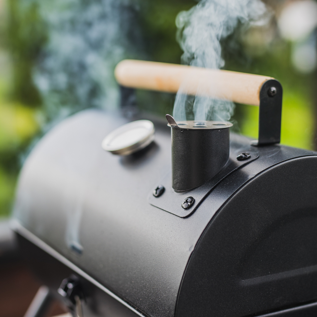 A meat smoker with the cover closed and vent hole open, showing smoke pouring from the vent.