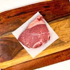 An American Wagyu sirloin steak, raw, on parchment paper on a wooden cutting board, set on a white marble countertop.