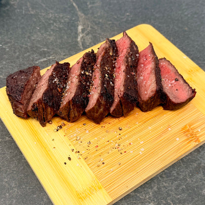 Sliced cooked American Wagyu Denver Steak on a wooden cutting board with a dark background