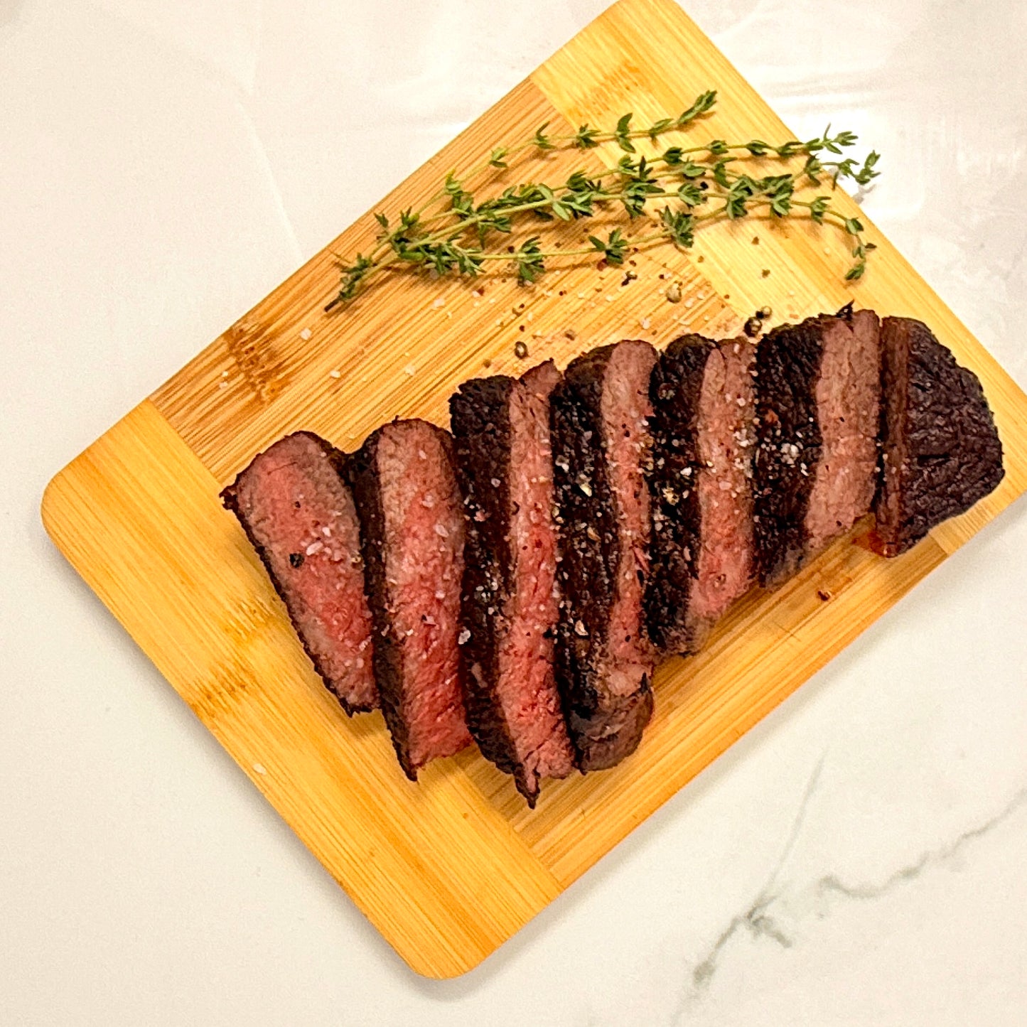 Sliced cooked American Wagyu Denver Steak on a wooden cutting board with fresh herbs